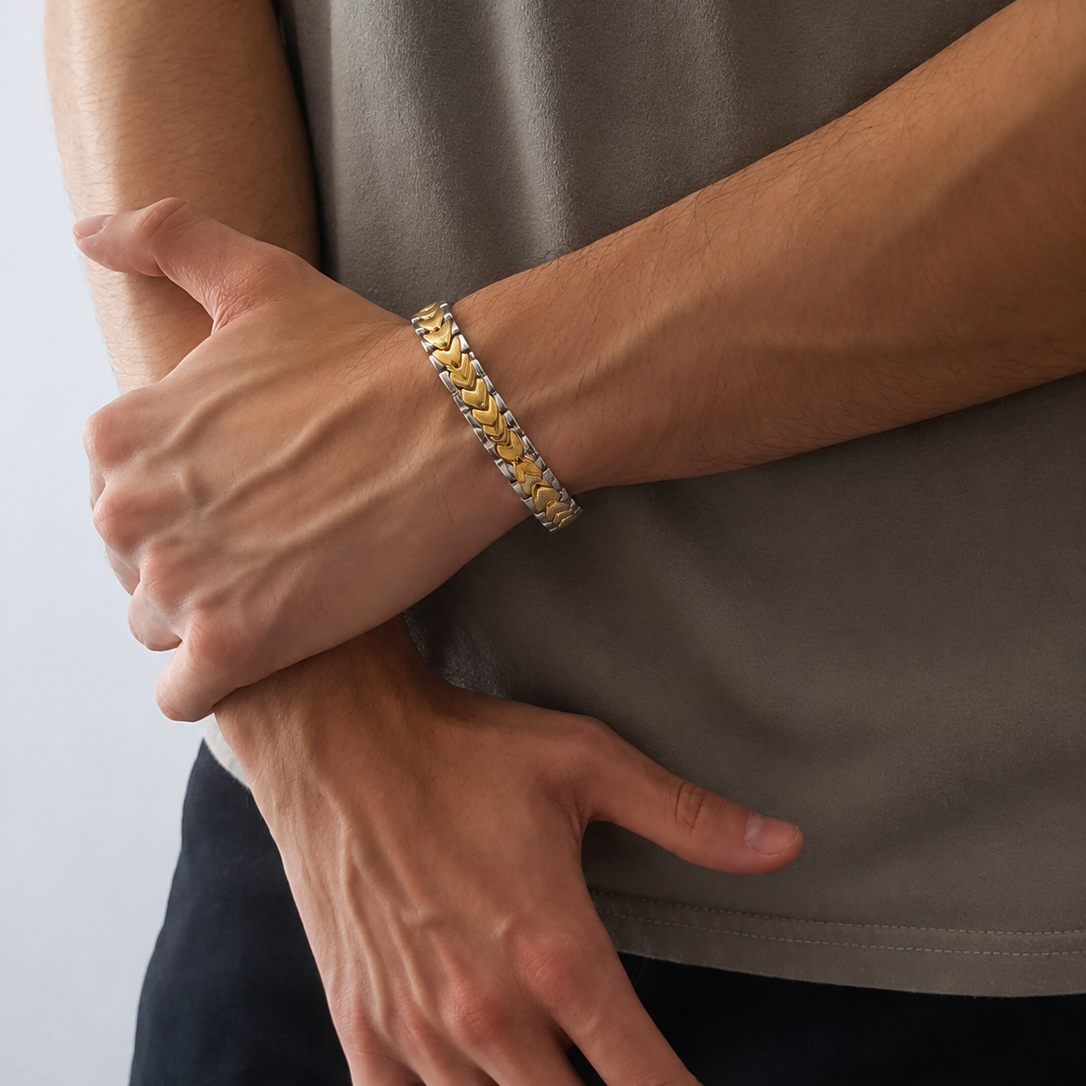 A close-up of a person wearing a gold and silver chain-link bracelet on their wrist, paired with a taupe-gray t-shirt and dark pants.