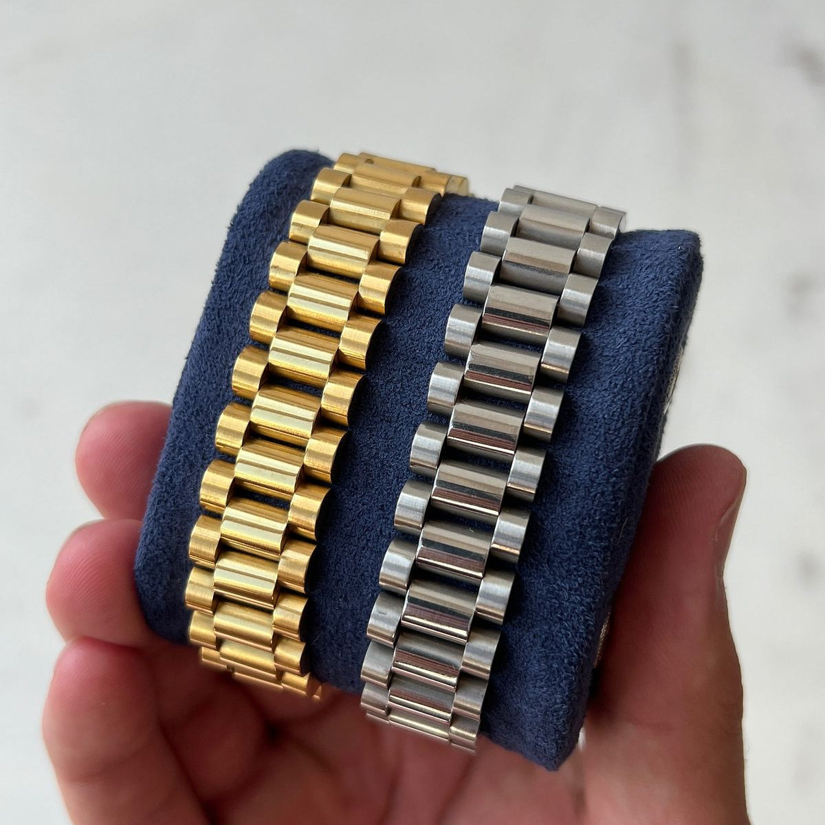 Two watch bracelets, one gold and one silver, held against a neutral background.