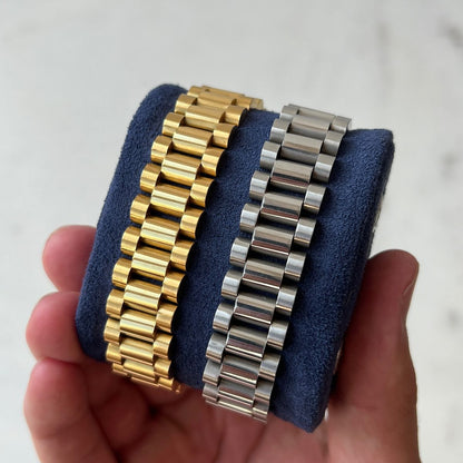Two watch bracelets, one gold and one silver, held against a neutral background.