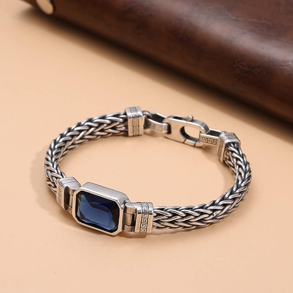 A sterling silver bracelet with a blue sapphire centerpiece, displayed against a beige background.