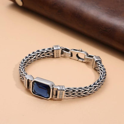 A sterling silver bracelet with a blue sapphire centerpiece, displayed against a beige background.