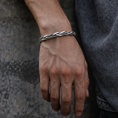 Hand wearing a braided silver bracelet against a textured gray background