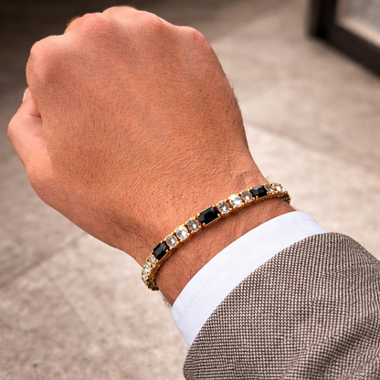 Hand wearing a gold bracelet with black and clear stones on a neutral background