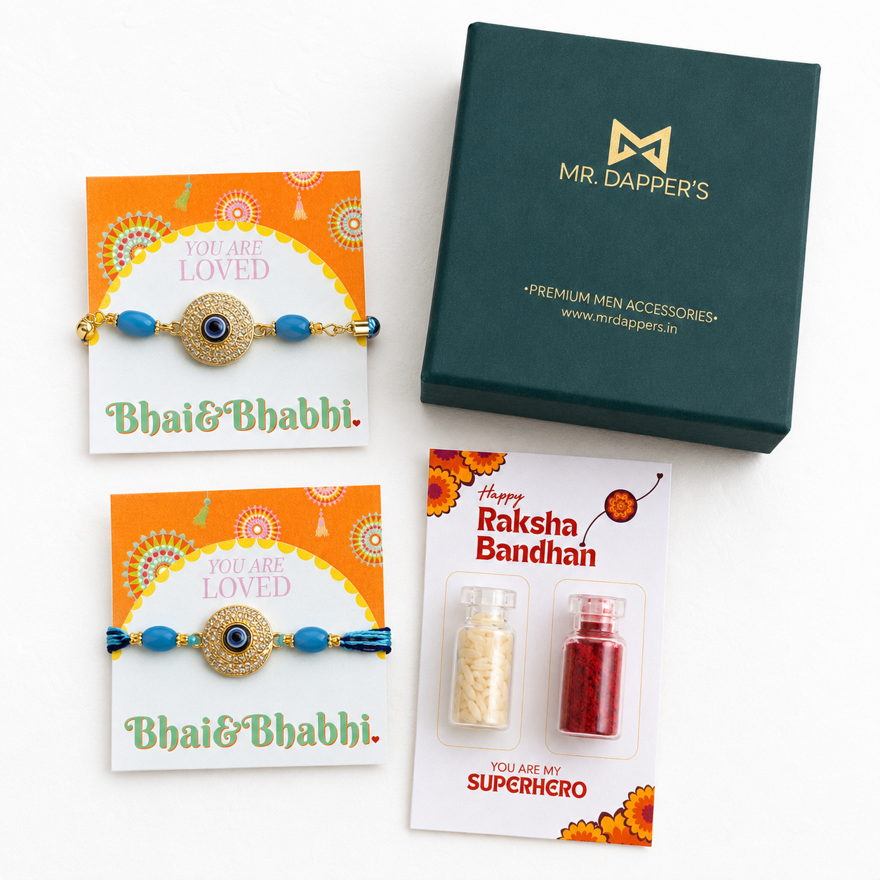 A Raksha Bandhan gift set by Mr. Dapper's on a white background, featuring two gold-plated rakhi bracelets with blue beads on orange and white cards, a dark green branded gift box, and a Raksha Bandhan card with two small bottles of thread.