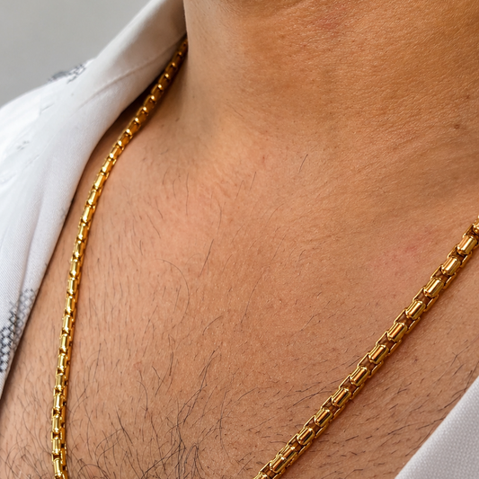 A close-up of a man's neck and chest wearing a thick, shiny gold chain necklace over a white shirt.