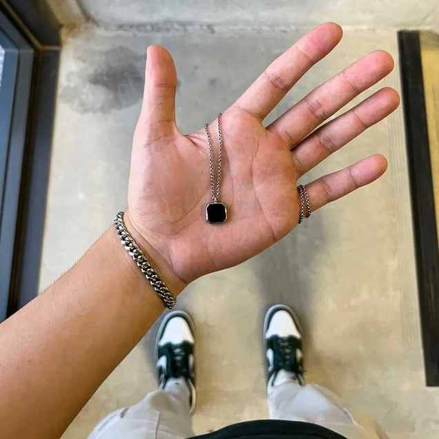 A person's hand holding a black onyx necklace with 925 sterling silver chain.