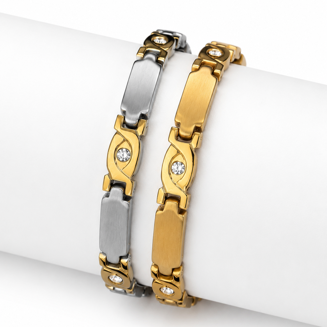 Two metal bracelets displayed on a white cylindrical wrist form. One bracelet is silver-toned with elongated rectangular links and small clear stones.