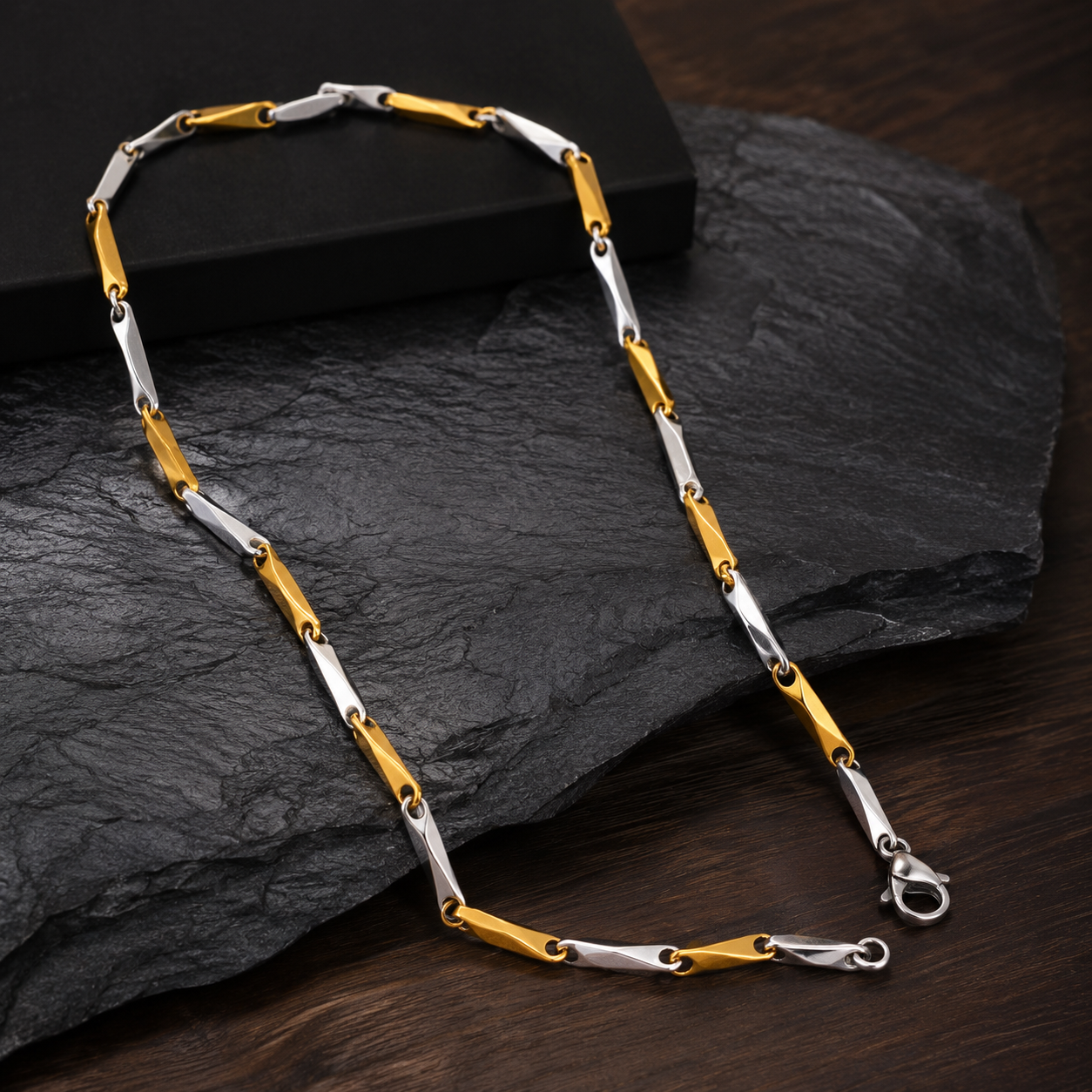 A two-tone chain necklace with alternating polished gold and silver links, displayed on a dark textured slate stone over a dark wooden surface.