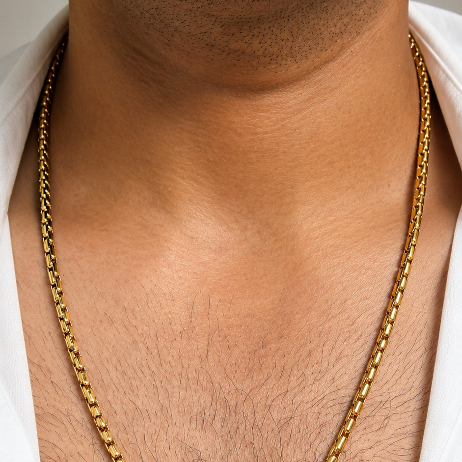 A close-up of a man's neck and chest wearing a gold chain necklace over a white shirt.