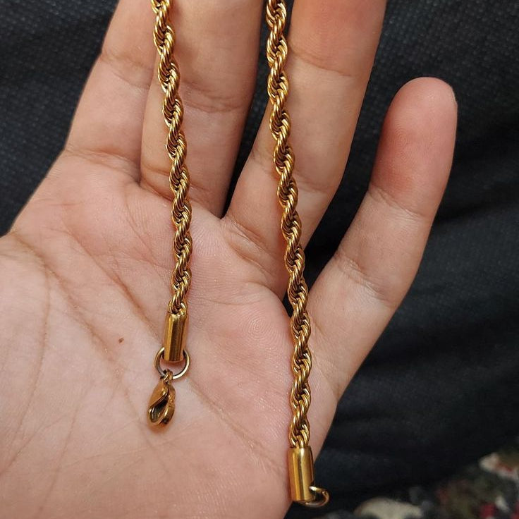 Gold rope chain held in a hand against a dark background
