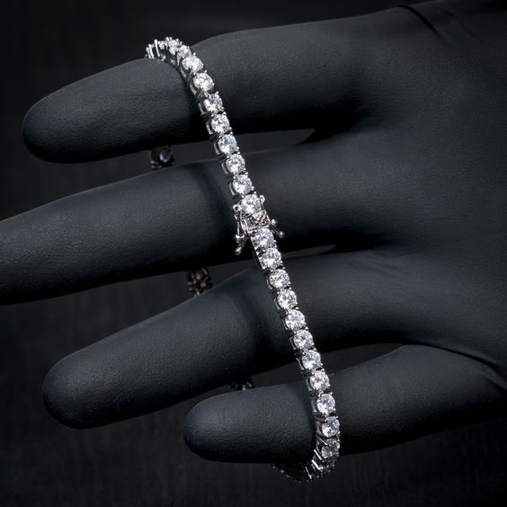 Silver bracelet with clear stones held by a gloved hand against a dark background