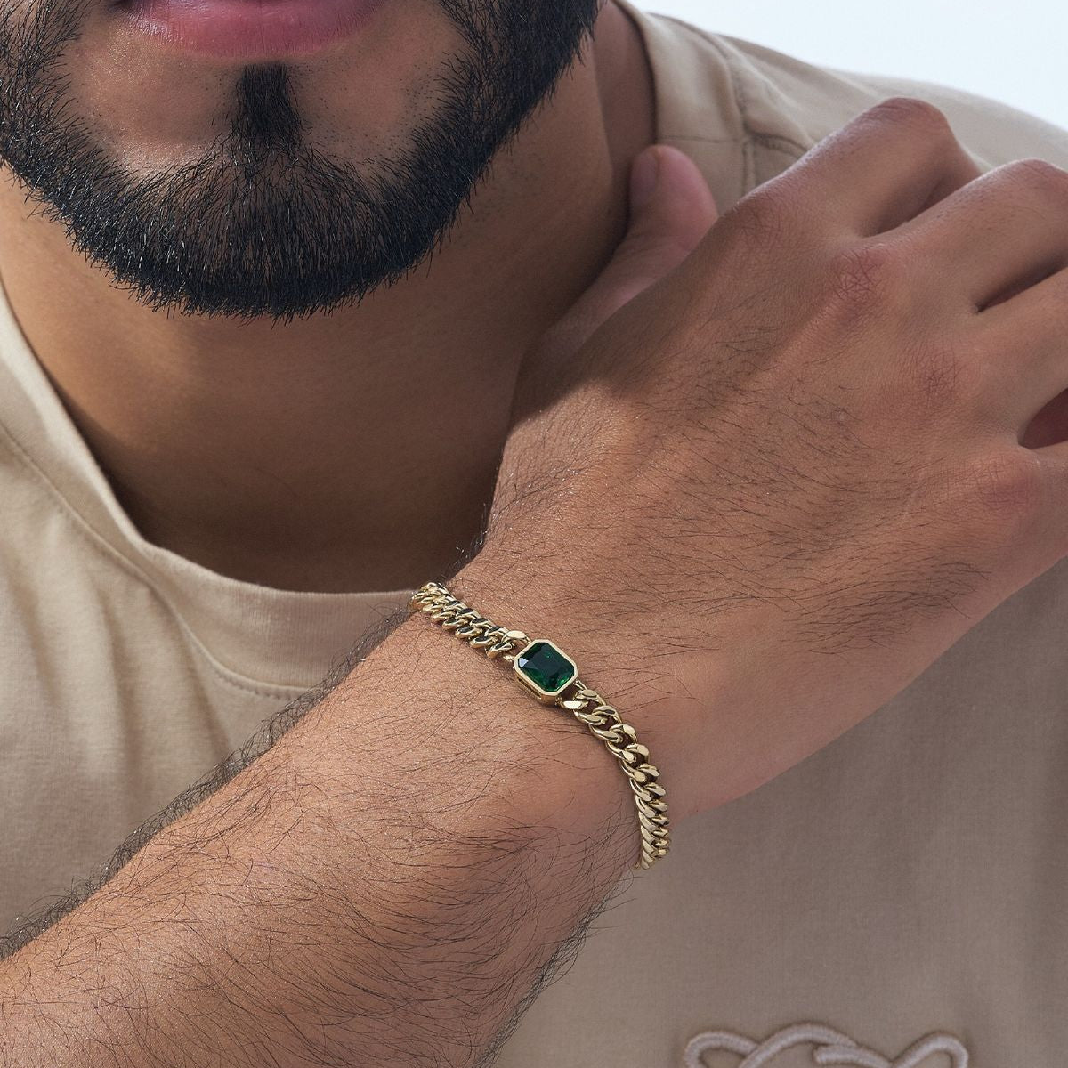 Man wearing a gold bracelet with a green gemstone on a neutral background