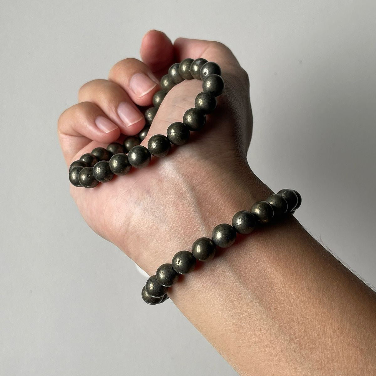 Hand wearing a black beaded bracelet on a plain background