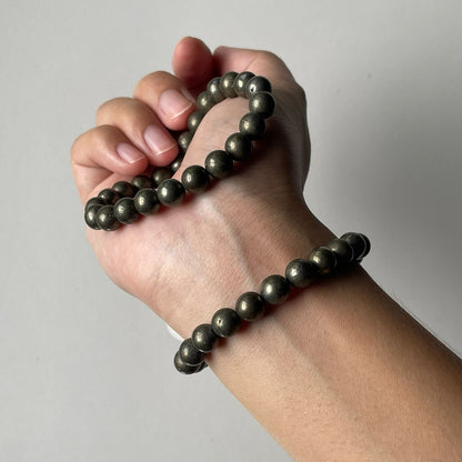 Hand wearing a black beaded bracelet on a plain background