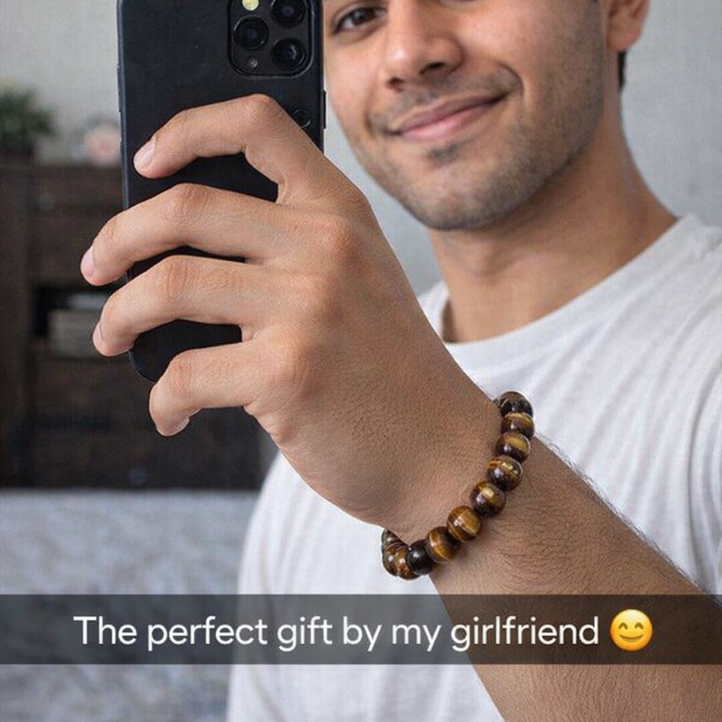 Man holding a phone with a bracelet on his wrist, smiling.