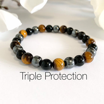 Beaded bracelet labeled 'Triple Protection' on a white surface with flowers in the background
